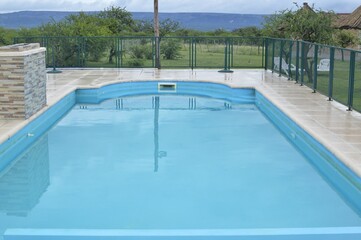 Blue pool filled with water with railings around it and mountains in the background