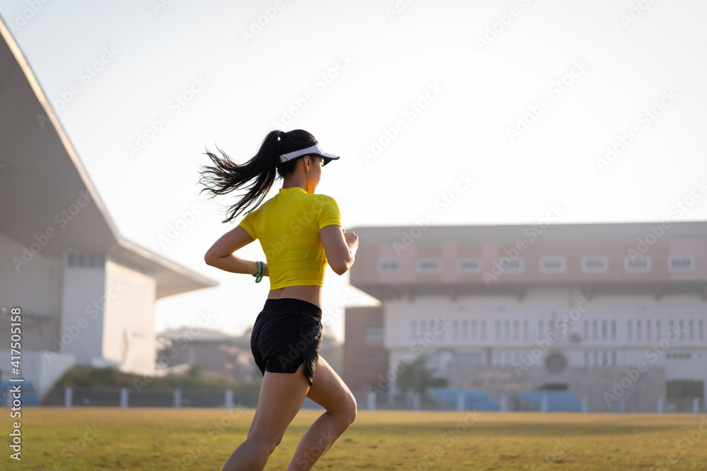 Wall mural a young asian woman athlete runner jogging on running track in city stadium in the sunny morning to 