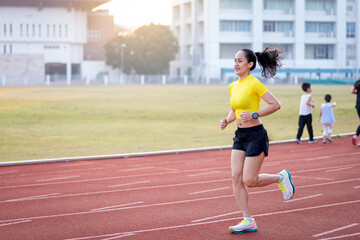 Obraz premium A young Asian woman athlete runner jogging on running track in city stadium in the sunny morning to keep fitness and healthy lifestyle. Young fitness woman runs on stadium track. Sport and recreation