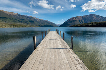 Obraz premium The jetty at Lake Rotoiti, Nelson Lakes National Park, New Zealand. Mountains and sky reflected in the lake.