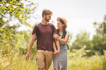 Outdoor activities. Young Caucasian couple walk marked route through national park. One day radial hike in summer. Two tourists with backpacks guy and girl joyful walk in an embrace outside the city