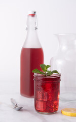 Cup of hibiscus tea in transparent cup on white tablecloth, decorated with mint and served with a slice of citrus and a spoon