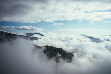 Wonderful alpine scenery with great rocks and mountains in dense low clouds. Atmospheric highlands landscape with mountain tops above clouds. Beautiful view to snow mountain peaks over thick clouds.