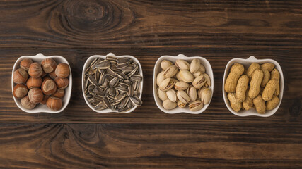 Four bowls of popular nuts and seeds on a wooden table. The view from the top.