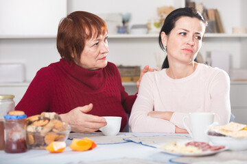 Portrait of sad mature woman talking with daughter at table with food