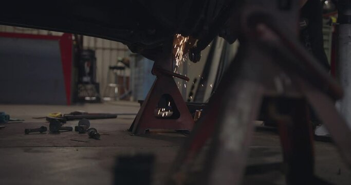 Grinding metal underneath a car in a mechanical workshop 4K slow motion cinematic 