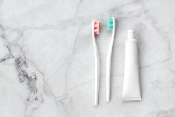 Two toothbrushes with pink and turquoise blue bristle and toothpaste on marble background. Dental and health care concept. Top view, flat lay. Free copy space.