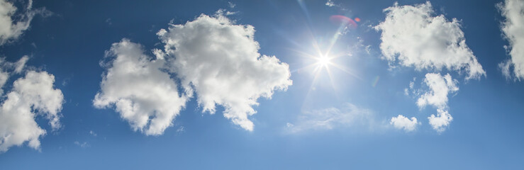 Naklejka na ściany i meble The sun shines on the blue sky among the white clouds, panoramic view