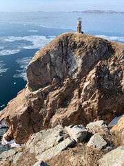 Fototapeta na wymiar Old lighthouse on rocky coast of the South-east coast of the island of Shkot in winter