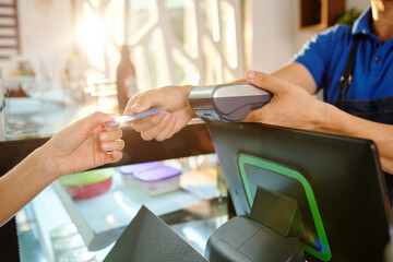 Hands of female customer giving credit card to barista when paying for coffee in coffeeshop