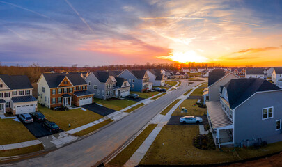 Suburban neighborhood street with newly constructed single family homes in an American  residential real estate development with stunning orange, pink, red, blue, yellow sunset - obrazy, fototapety, plakaty