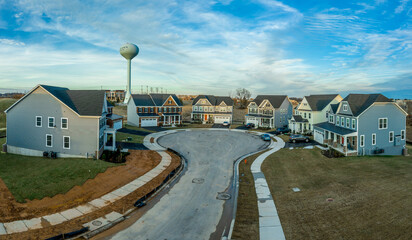 Aerial view of seven single family homes covered with blue, white, beige vinyl or brick façade surrounding in semi circle a dead end neighborhood street,  American residential community , water tower 