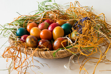 Coloreful eggs for Easter in a basket with raffia on a white background