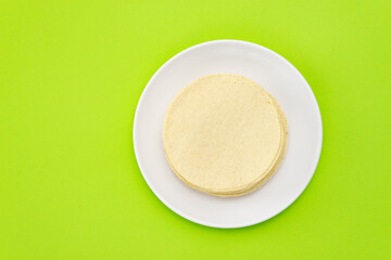 medio kilo de tortillas de maíz mexicanas para tacos, quesadillas y demás platillos de méxico, encima de un plato blanco limpio, fondo verde, vida saludable