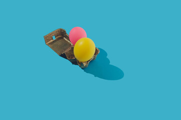 Colorful balloons in egg cardboard, creative Easter concept on blue background.
