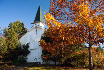 An old white U.S. Army base chapel in autumn with maple trees and a blue sky.