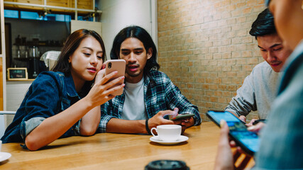 Group of happy young Asia friends having fun a great time and using smartphone together while sitting together at cafe restaurant. Coffee shop holiday activity, modern friendship lifestyle concept. © tirachard