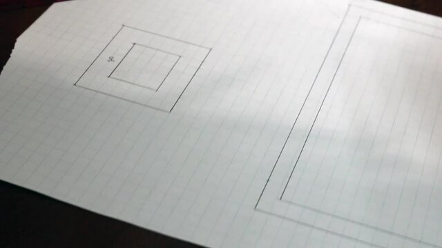 A woman uses a pen to sketch out a floor plan for a house on square graph paper using a clear red ruler on a hardwood mahogany desk, Canada, 2021. 