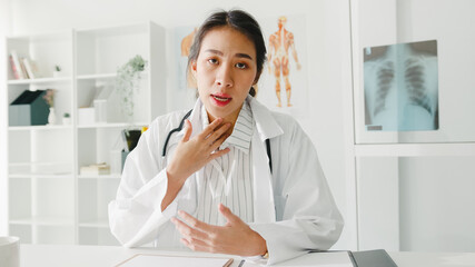 Young Asia lady doctor in white medical uniform with stethoscope using computer laptop talk video conference call with patient, looking at camera in health hospital. Consulting and therapy concept.
