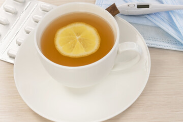 Close-up of a white cup with lemon tea on the background of a thermometer and pills in a blister. The concept of virus prevention and treatment.