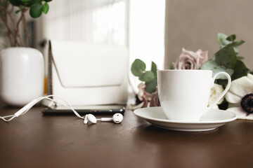 Cup of coffee, bouquet of anemone, purple roses, woman handbag, phone on table