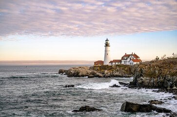 Fototapeta na wymiar Lighthouse on a cliff top against a cloudy sky on the Atlantic coast in Portland Maine in New England