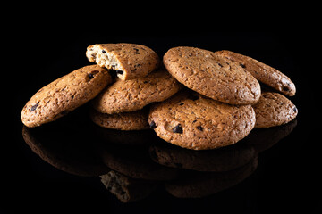 Oatmeal cookies with chocolate chips are isolated on a black background with a reflection. Lots of brown round homemade cookies lying on a reflective surface, close-up