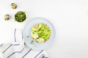 Toast with egg, avocado and micro greens on a white wooden background. Healthy breakfast, plant based food. Flat lay, top view. 