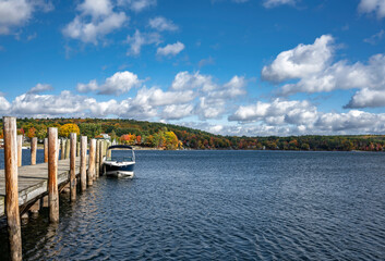Fototapeta na wymiar Pleasure motor boat is moored at a wooden pier on a picturesque lake with autumn trees in the hills in Maine