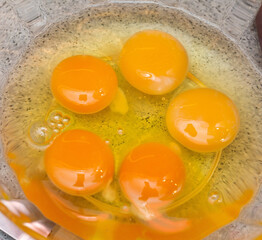 Five raw eggs in a glass bowl close-up top view. Round yellow tails, transparent squirrel. The bowl is on the table. 