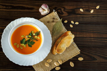 Vegetarian pumpkin cream soup in a white bowl decorated with seeds and herbs on a light background