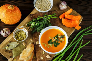 Vegetarian pumpkin cream soup in a white bowl decorated with seeds and herbs on a light background