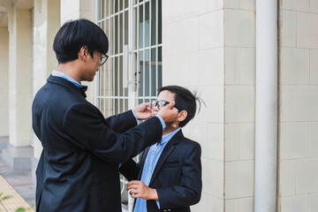 Asian big brother with vintage suit help his little brother put on a glasses
