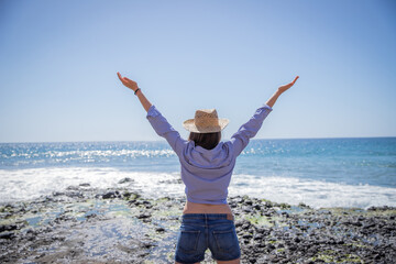 girl on vacation opens her arms and looks at the ocean, she is happy and free and enjoying her holidays