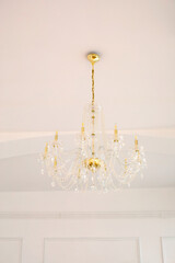 From below of classic elegant golden chandelier with crystal pendants hanging on white ceiling in light room