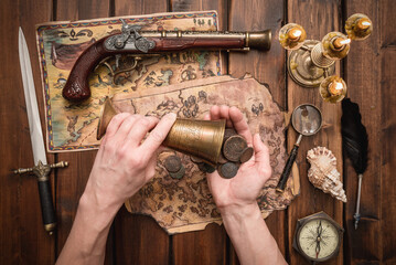 Ancient treasure coins in a goblet in pirate hand concept. Old treasure map on the table.