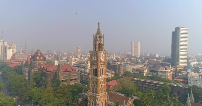 Drone shot of the Rajabai Clock Tower next to the Bombay High Court Building and Oval Maidan, an ornate 1878 clock tower modeled after Big Ben and featuring stained-glass windows and musical chimes