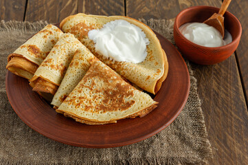 Stack of pancakes or crepes on a plate served with sour cream. Traditional food for the Russian pancake week. Wooden background