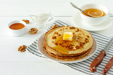 Pancakes served with honey syrup and butter on a white plate. Traditional crepes for pancake week or Shrovetide.