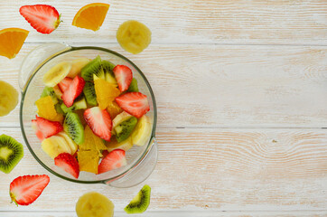fresh healthy summer fruit salad in a glass bowl with pieces of  orange kiwi strawberry and banana fitness nutrition diet vegetarianism and food for a slim figure