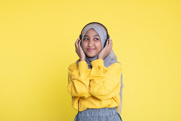 attractive asian woman listening music on yellow background. Woman wearing headset.