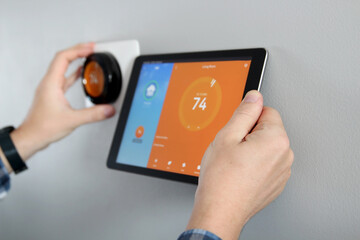 Man is Adjusting a  temperature using a tablet with a smart home app in modern living room - obrazy, fototapety, plakaty