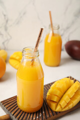 Bottles of fresh mango juice on light background