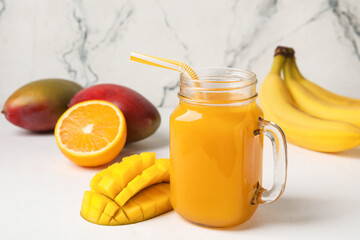 Mason jar of fresh juice and  tropical fruits on light background