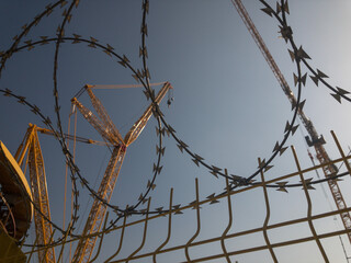 Huge construction crane behind barbed wire fence