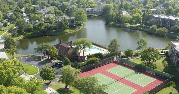 Aerial view of a neighborhood with pool, tennis courts and lake during summer.