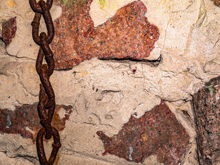 Old rusty iron chain on the background of a granite wall. Links of a metal chain. Grant wall....