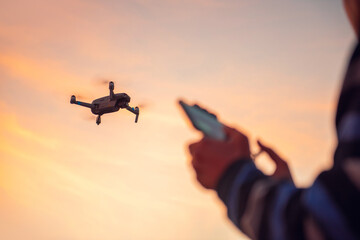 Closeup drone and blurred man operating a drone with remote control in sunset.