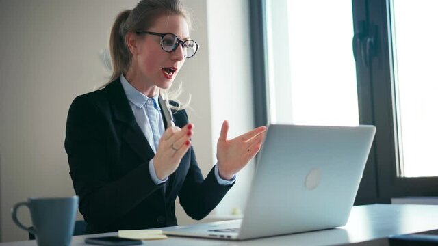 An angry woman boss in glasses and a jacket scolds subordinates via video conference while working from home.