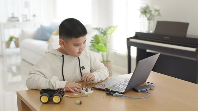 Young asia student remotely learn online at home in coding robot car and electronic board cable in STEM, STEAM, mathematics engineering science technology computer code in robotics for kids concept.
